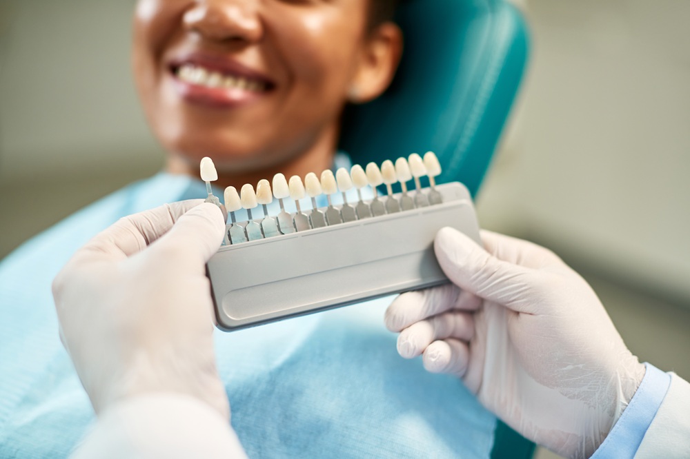 Teeth Shade Matching for Veneers - Dentist St Paul MN A dentist wearing gloves holds a shade guide to match the perfect tooth color for a smiling patient seated in a dental chair. - Dentist St Paul MN