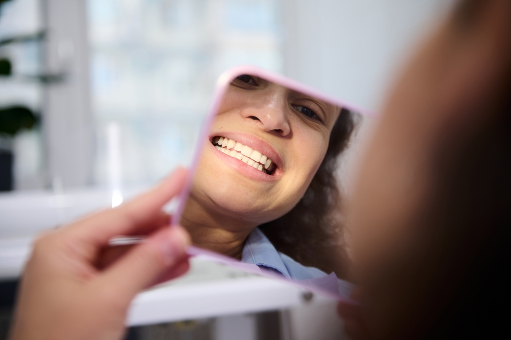 Close-up reflection in the cosmetic mirror of a pretty woman, female patient sitting in dental chair