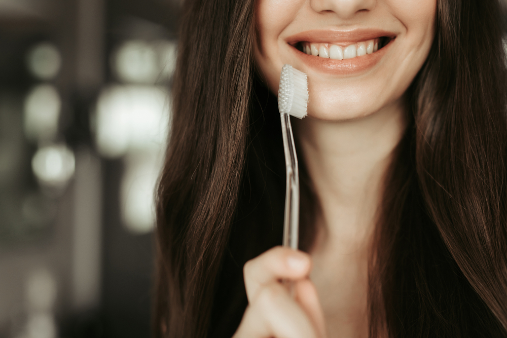 Close up young female smile. She holding dental cleaning brush in hand. Tooth care concept
