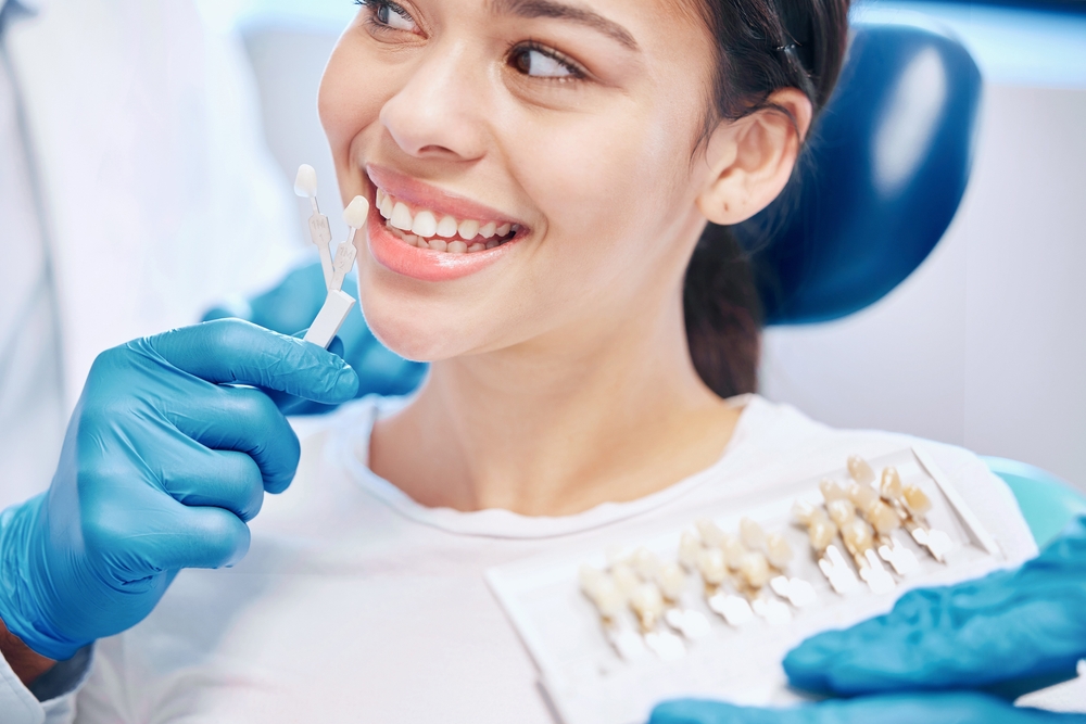 Smiling woman evaluating dental veneer color samples with dentist during cosmetic consultation – Dental Veneers Highland Park