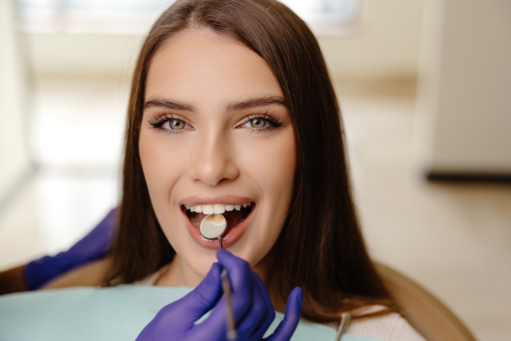 Happy girl is sitting at dentist chair in modern clinic and smiling. Patient enjoying dental treatment with professional dentist.