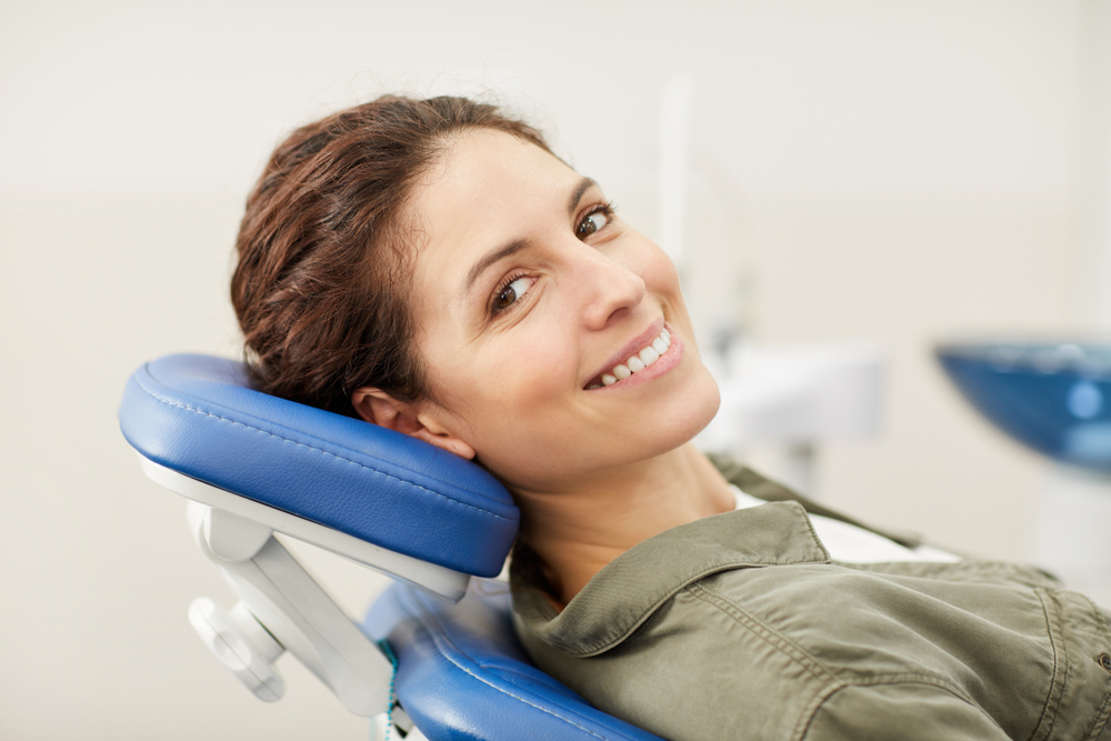 Portrait of smiling young woman lying in dental chair and looking at camera, copy space