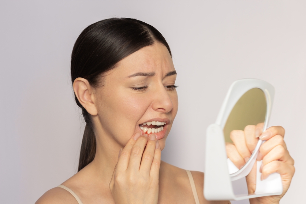 Female patient examining her gums in handheld mirror showing early signs of gum disease – Gum Disease Treatment Highland Park