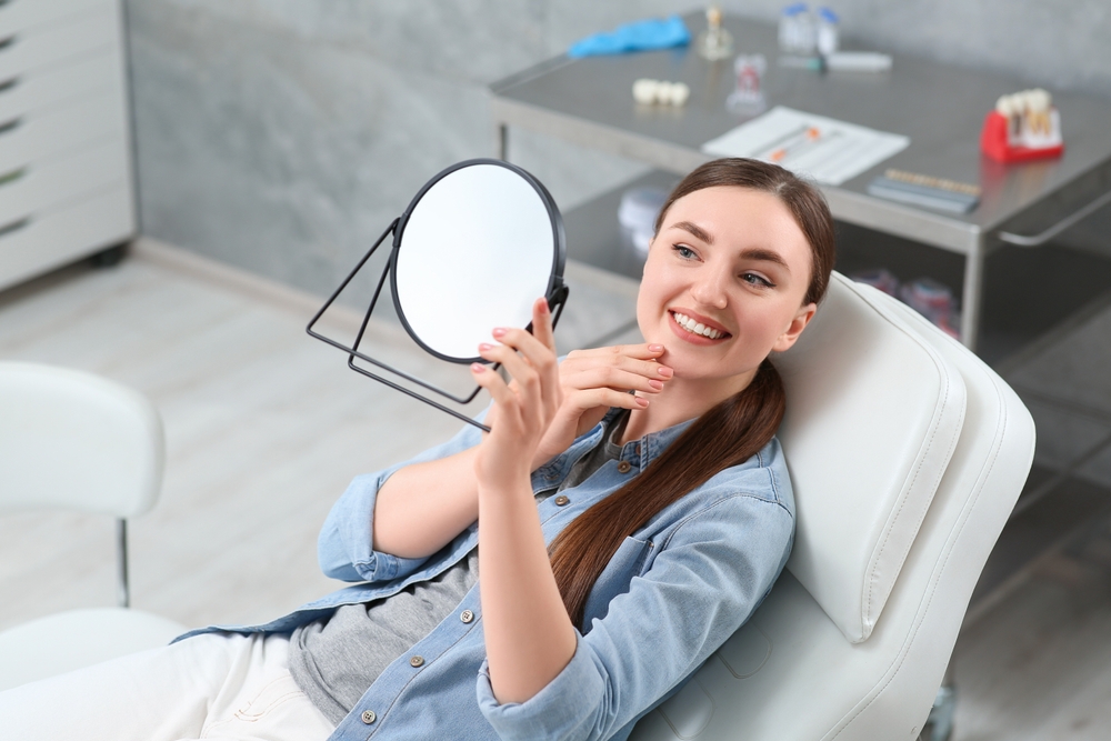 Young woman looking at her new dental implants in mirror indoors